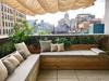 A custom built-in cedar bench topped with cushions and pillows sits overlooks the New York City skyline.